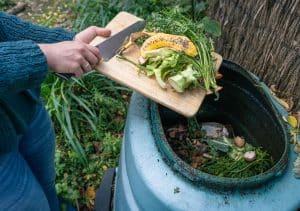 Woman Disposing of Biodegradable Kitchen Waste into a Large Compost Bin in the Garden