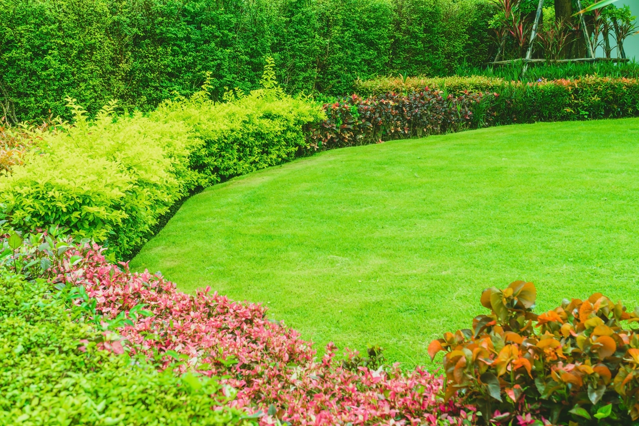 A landscaped formal front yard with green Bermuda grass and various flowers.